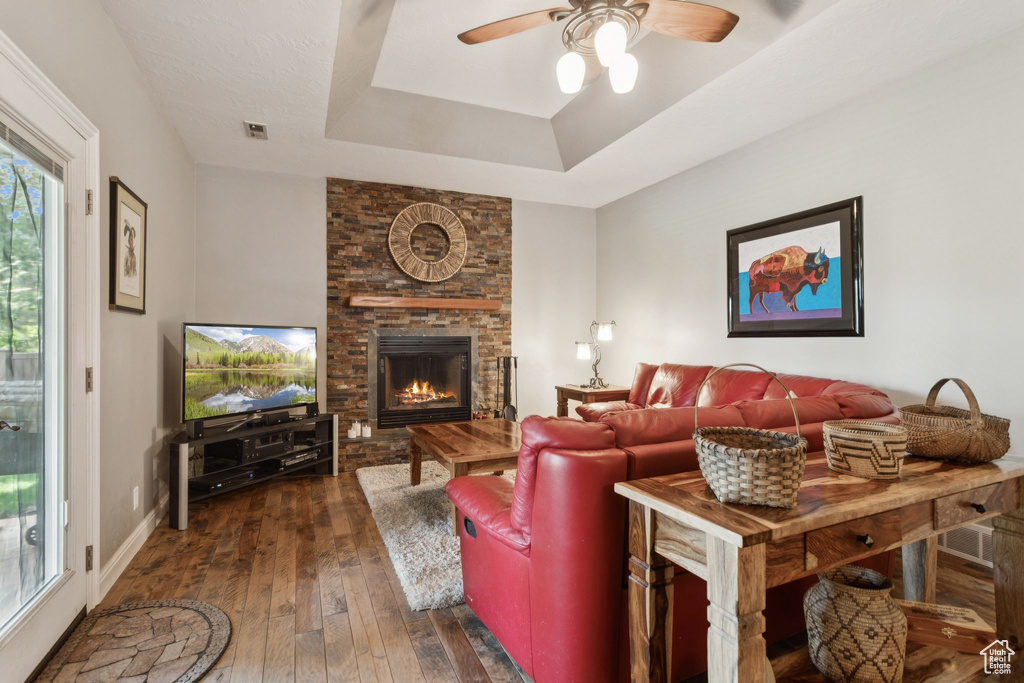 Living room featuring a ceiling fan, dark wood finished floors, a fireplace, and a tray ceiling
