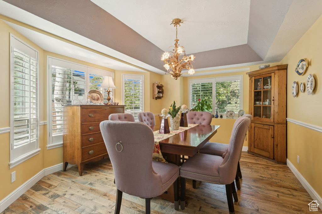 Dining space featuring light wood-type flooring, a tray ceiling, baseboards, and a chandelier