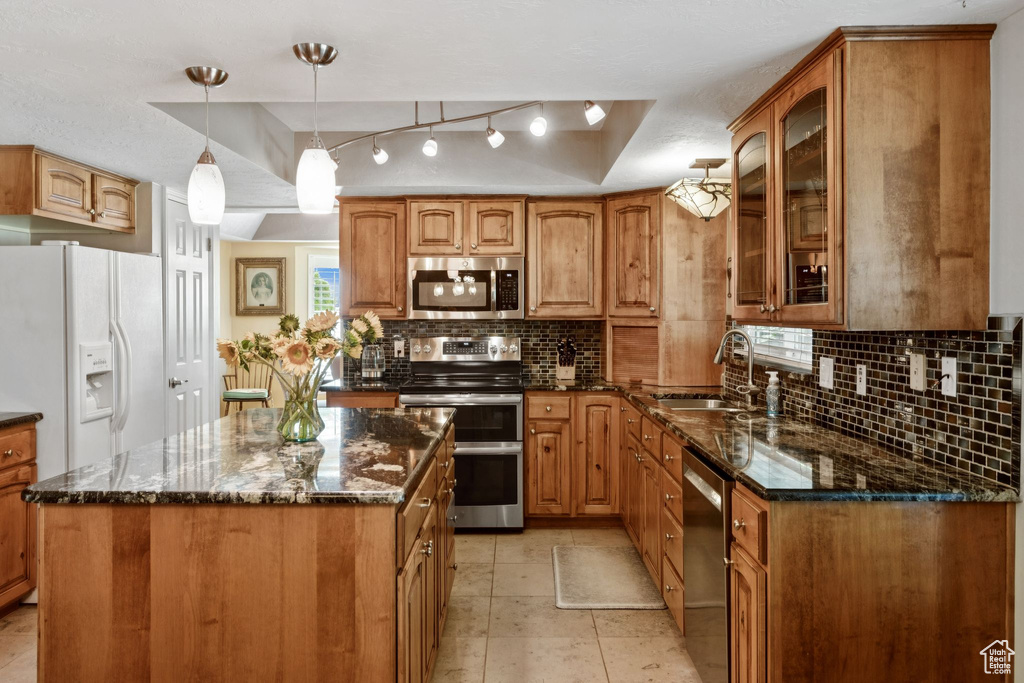 Kitchen featuring stainless steel appliances, a sink, glass insert cabinets, dark stone countertops, and backsplash