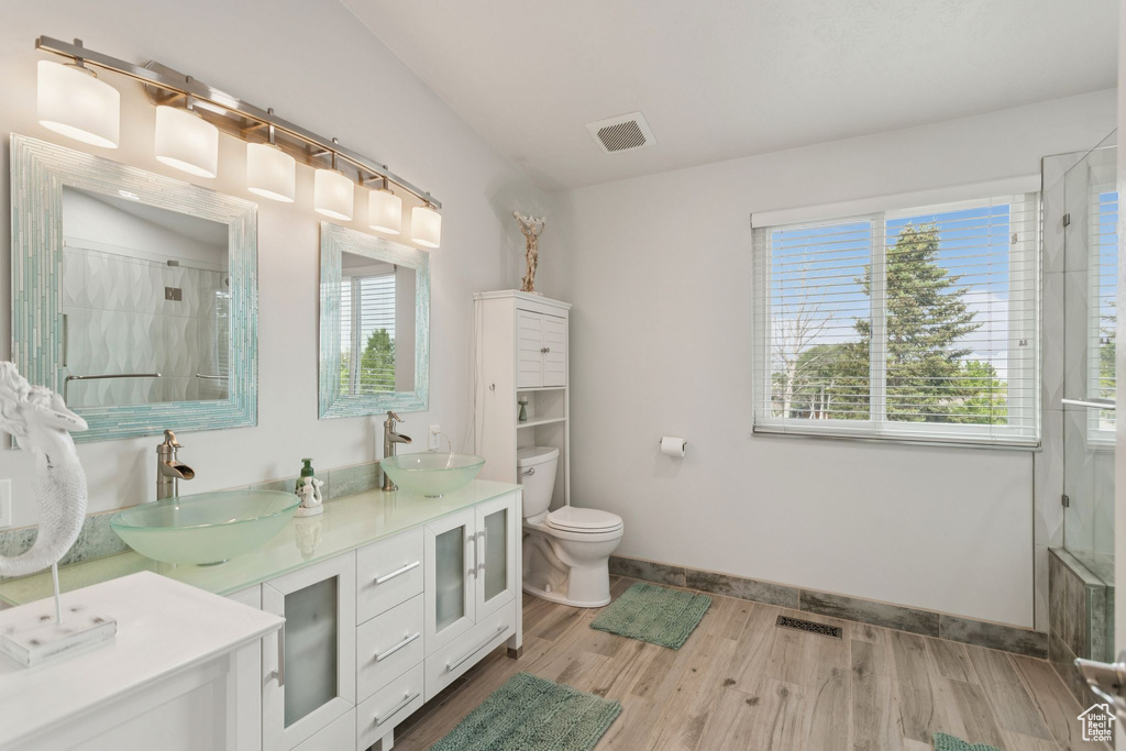 Full bath featuring toilet, wood finished floors, double vanity, baseboards, and a shower