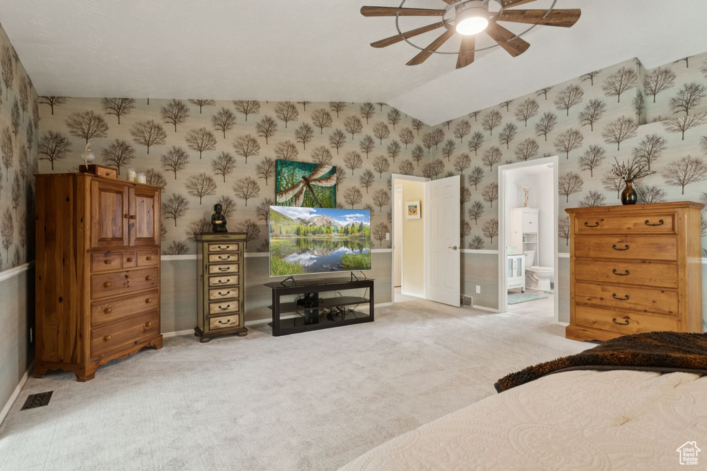 Bedroom featuring wallpapered walls, lofted ceiling, light colored carpet, connected bathroom, and a ceiling fan