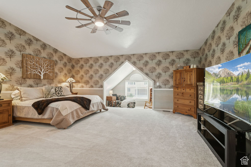 Bedroom featuring wallpapered walls, wainscoting, light colored carpet, a ceiling fan, and vaulted ceiling