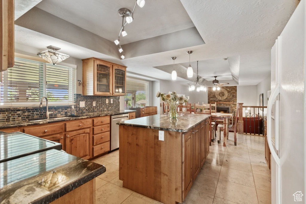 Kitchen featuring a raised ceiling, stainless steel dishwasher, tasteful backsplash, ceiling fan, and a kitchen island