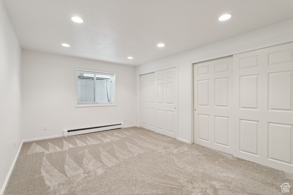Unfurnished bedroom featuring a baseboard radiator, multiple closets, carpet, recessed lighting, and baseboards