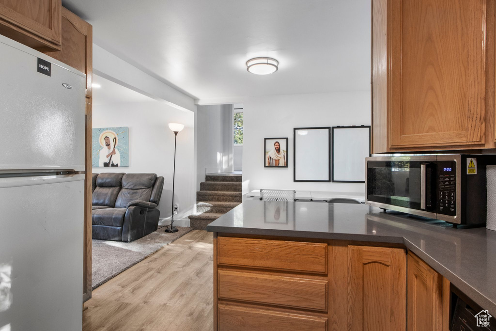 Kitchen featuring freestanding refrigerator, stainless steel microwave, open floor plan, light wood-type flooring, and a peninsula
