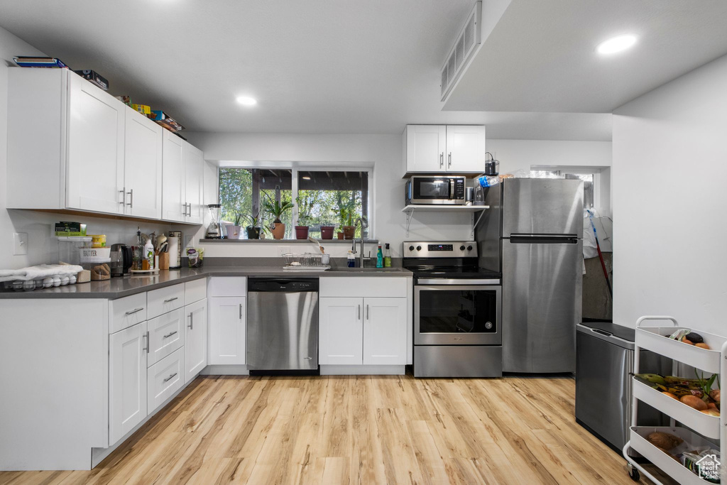 Kitchen with stainless steel appliances, dark countertops, white cabinets, light wood finished floors, and recessed lighting