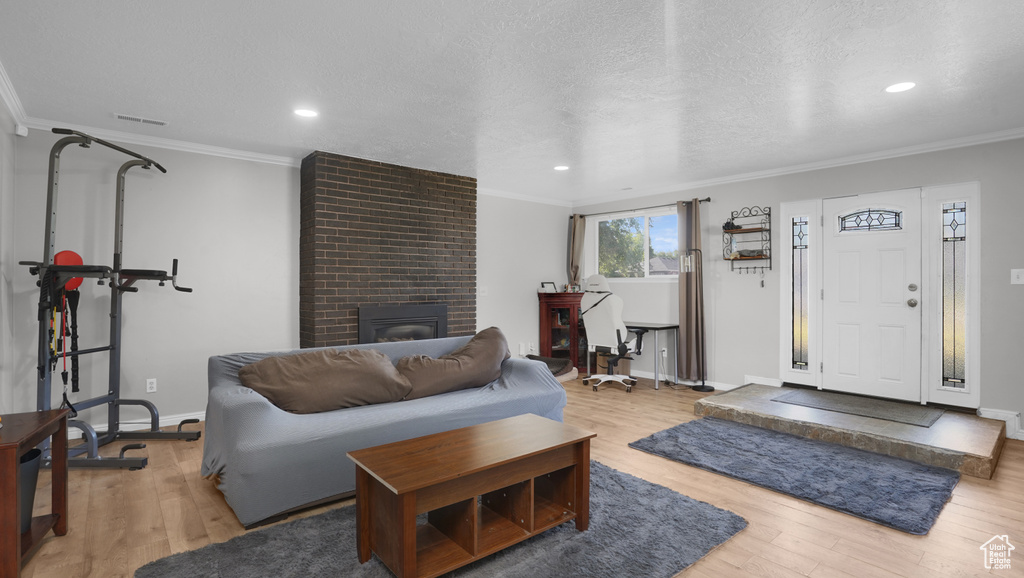 Living room featuring crown molding, baseboards, light wood finished floors, a brick fireplace, and recessed lighting