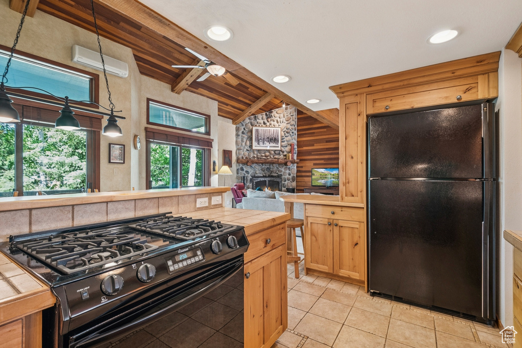 Kitchen featuring black appliances, an AC wall unit, a fireplace, wood walls, and light tile patterned flooring