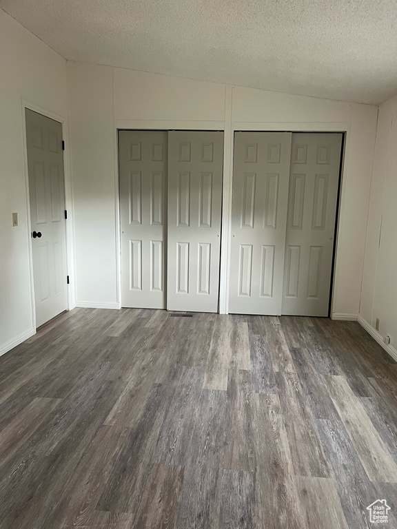 Unfurnished bedroom featuring wood finished floors, a textured ceiling, and two closets