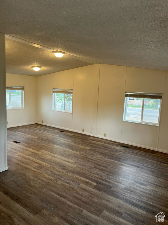 Spare room featuring a textured ceiling, healthy amount of natural light, dark wood-style floors, and baseboards