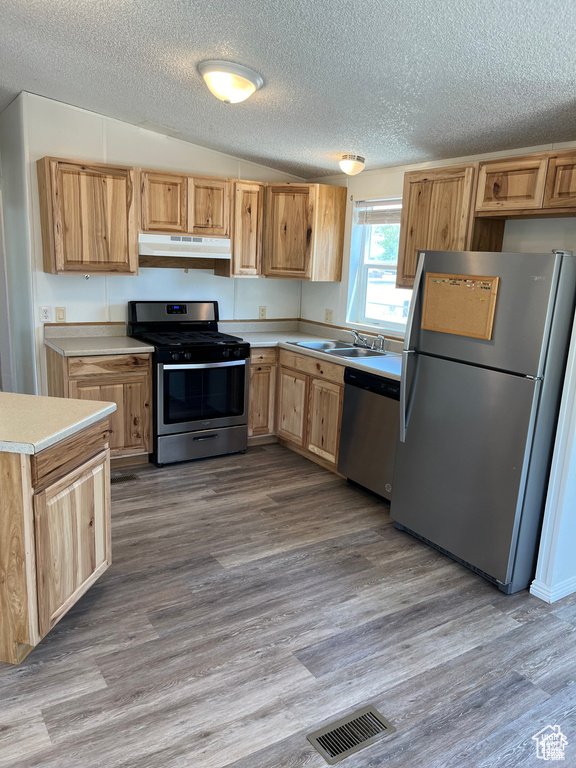 Kitchen featuring stainless steel appliances, under cabinet range hood, a sink, light countertops, and a textured ceiling