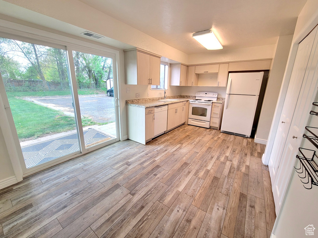 Kitchen with white appliances, light wood-style flooring, light countertops, and a sink