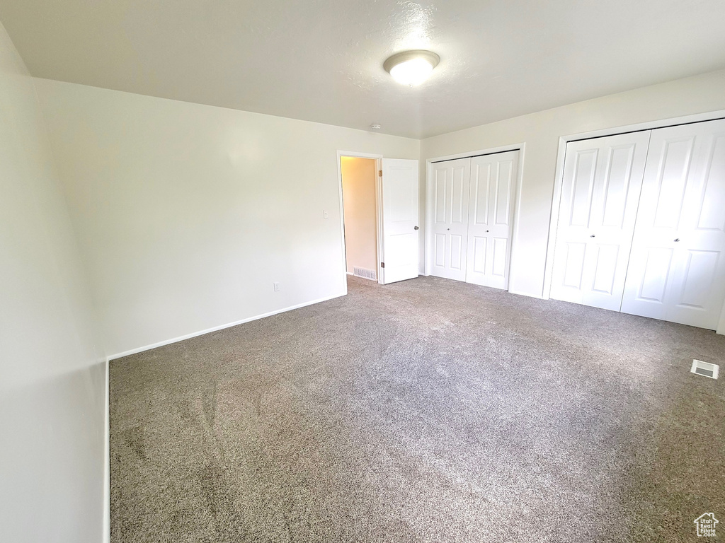 Unfurnished bedroom with two closets, carpet flooring, and baseboards