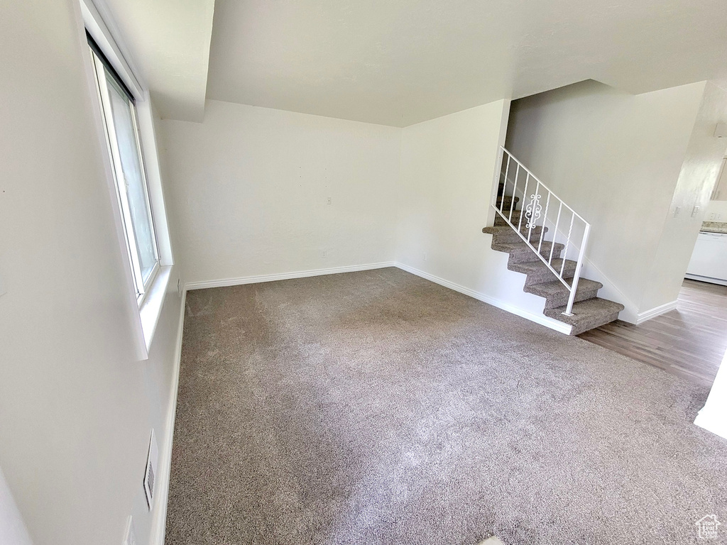 Unfurnished living room featuring carpet, stairs, and baseboards