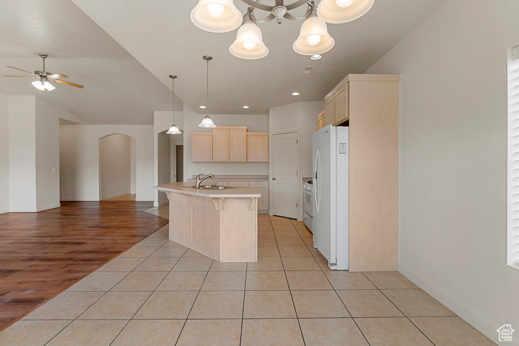 Kitchen featuring open floor plan, white appliances, light brown cabinetry, and a sink