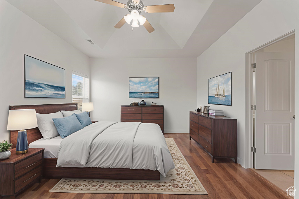 Bedroom featuring wood finished floors, a raised ceiling, and ceiling fan