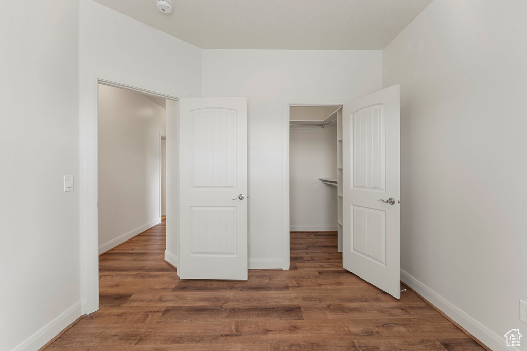 Unfurnished bedroom featuring wood finished floors, baseboards, a walk in closet, and a closet