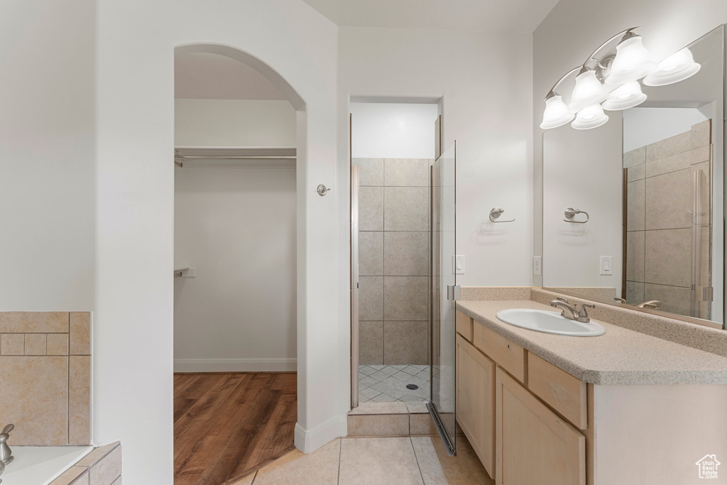 Bathroom with vanity, a walk in closet, a shower stall, wood finished floors, and a bathtub