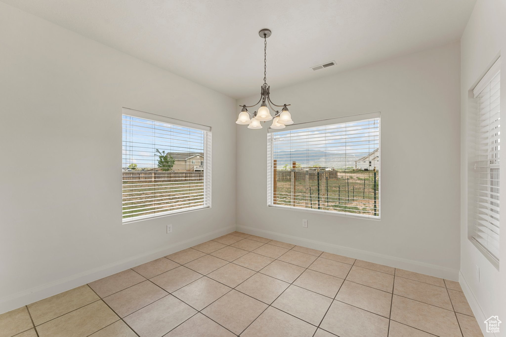 Spare room featuring a chandelier, healthy amount of natural light, and light tile patterned floors
