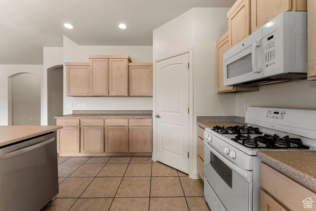 Kitchen featuring white appliances, light brown cabinetry, light tile patterned flooring, arched walkways, and recessed lighting