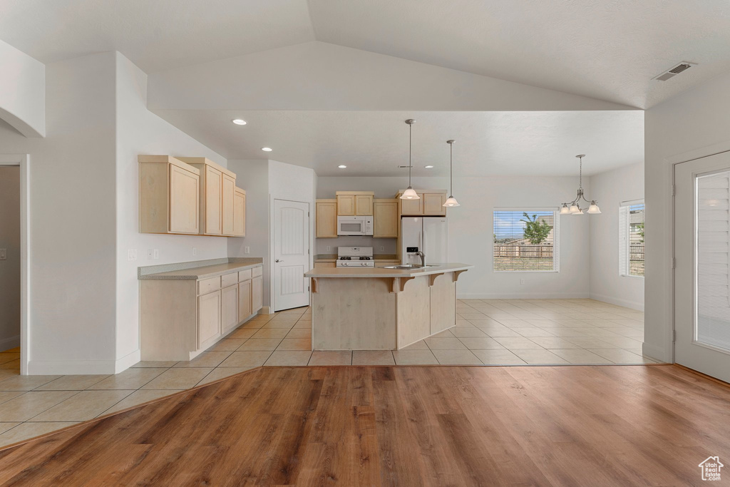 Kitchen with white appliances, lofted ceiling, light brown cabinetry, light wood-style flooring, and light countertops