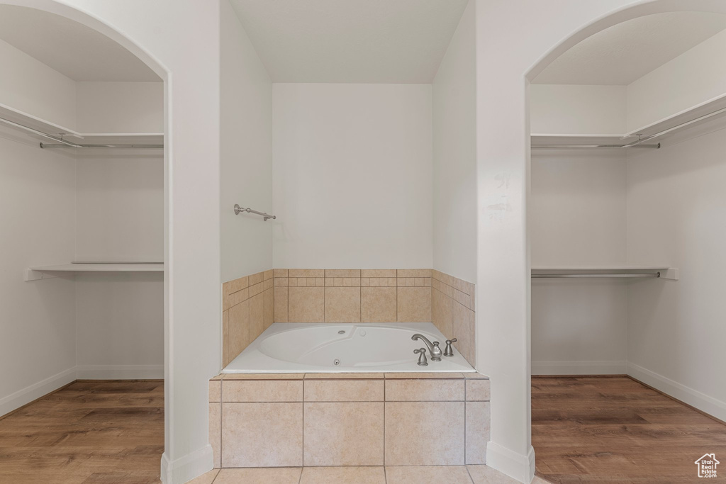 Full bathroom with a jetted tub, a walk in closet, and wood finished floors