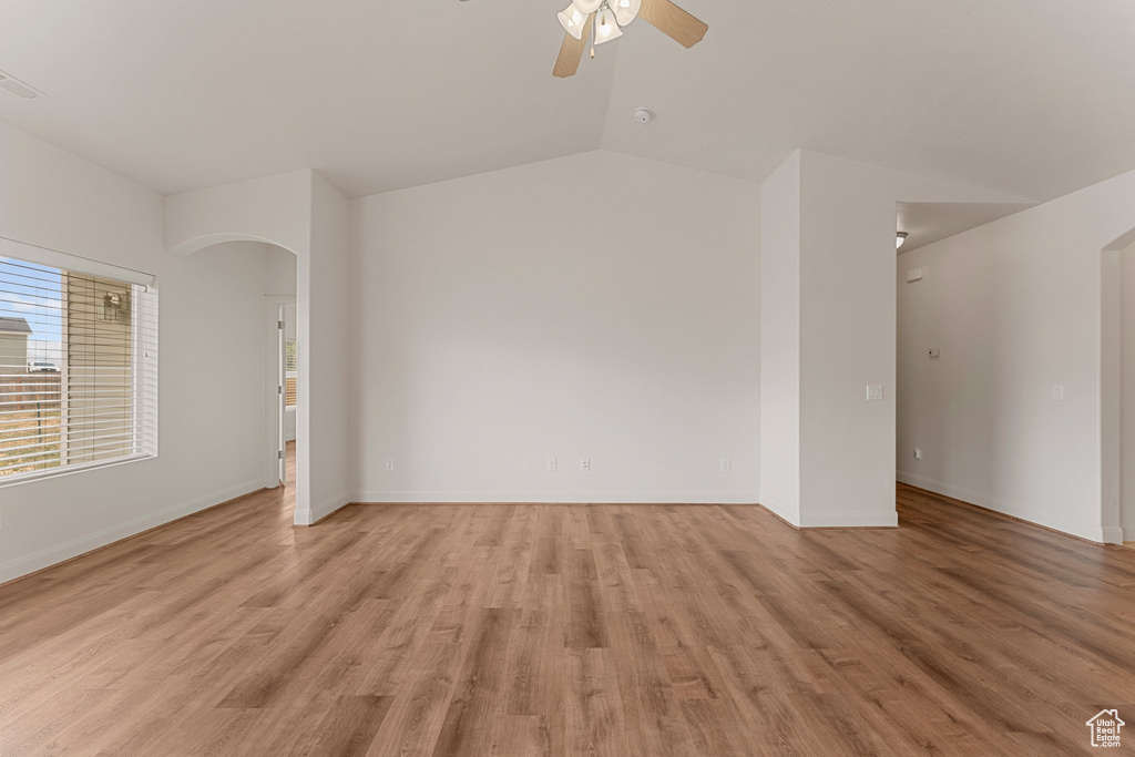Unfurnished room featuring arched walkways, ceiling fan, light wood-style flooring, baseboards, and vaulted ceiling