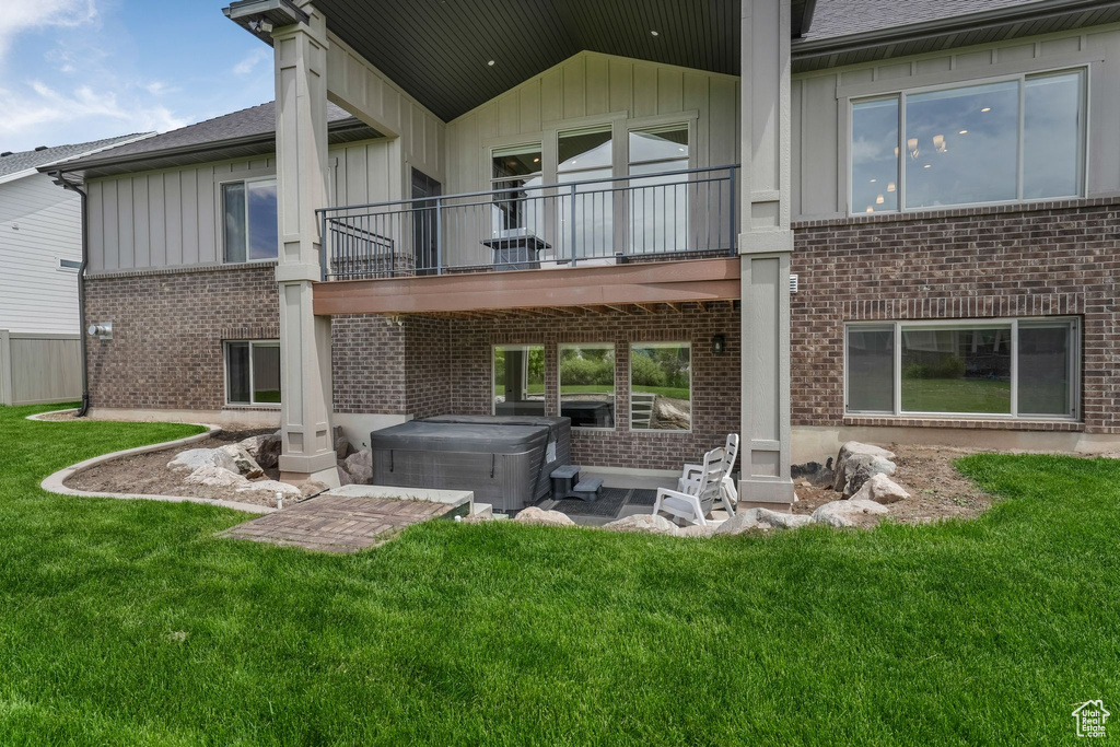 Rear view of house featuring a hot tub, a balcony, brick siding, a lawn, and a patio