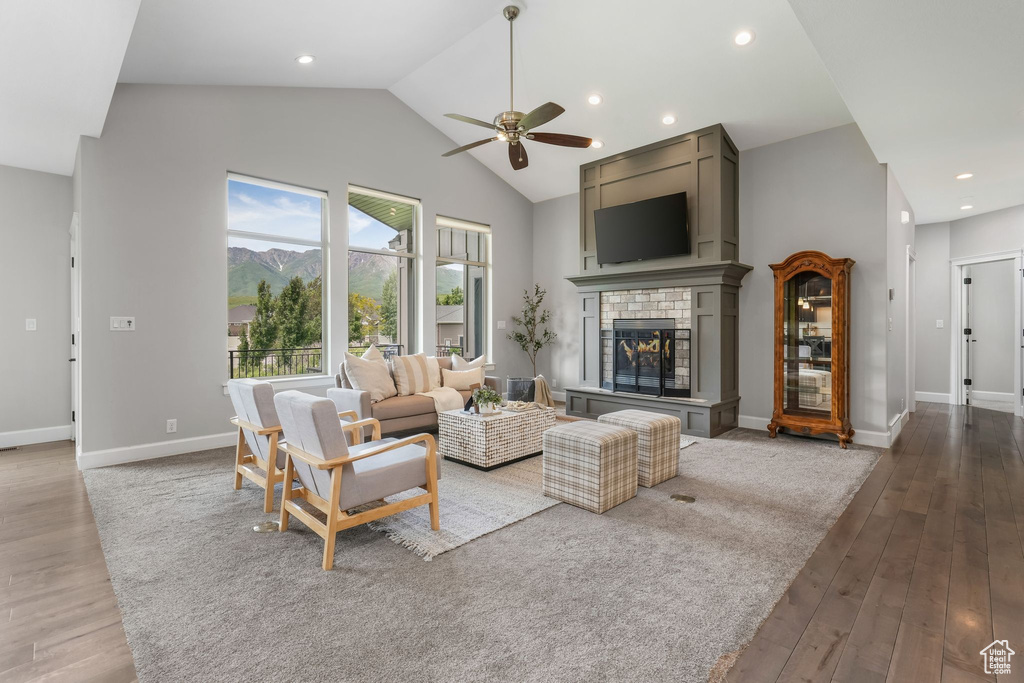 Living room featuring high vaulted ceiling, ceiling fan, wood finished floors, a brick fireplace, and baseboards