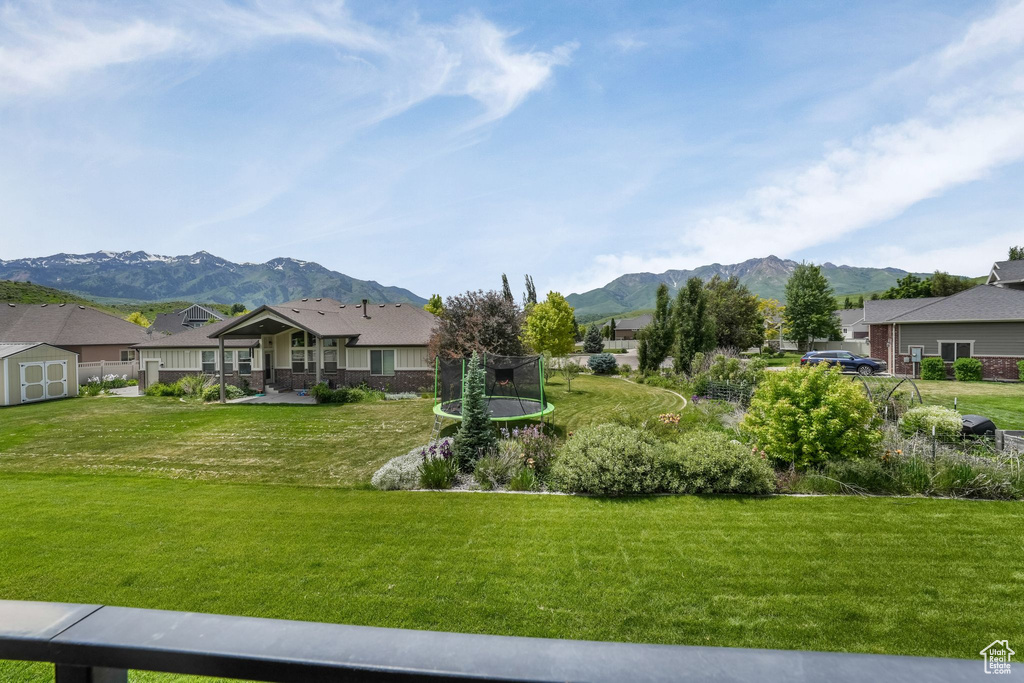 View of grassy yard with a trampoline, a mountain view, and a residential view