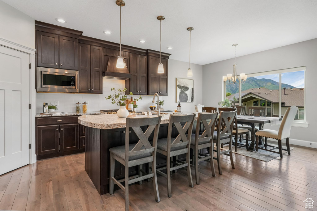 Kitchen with stainless steel microwave, dark brown cabinets, light wood-style floors, a kitchen bar, and custom exhaust hood