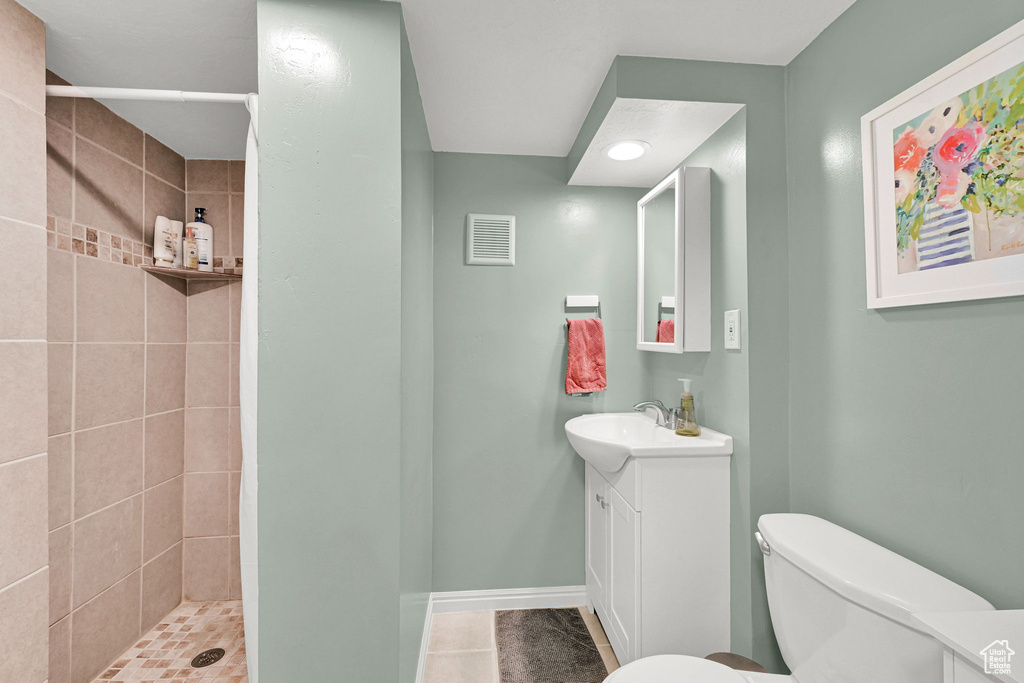 Full bathroom with vanity, tile patterned flooring, toilet, tiled shower, and baseboards