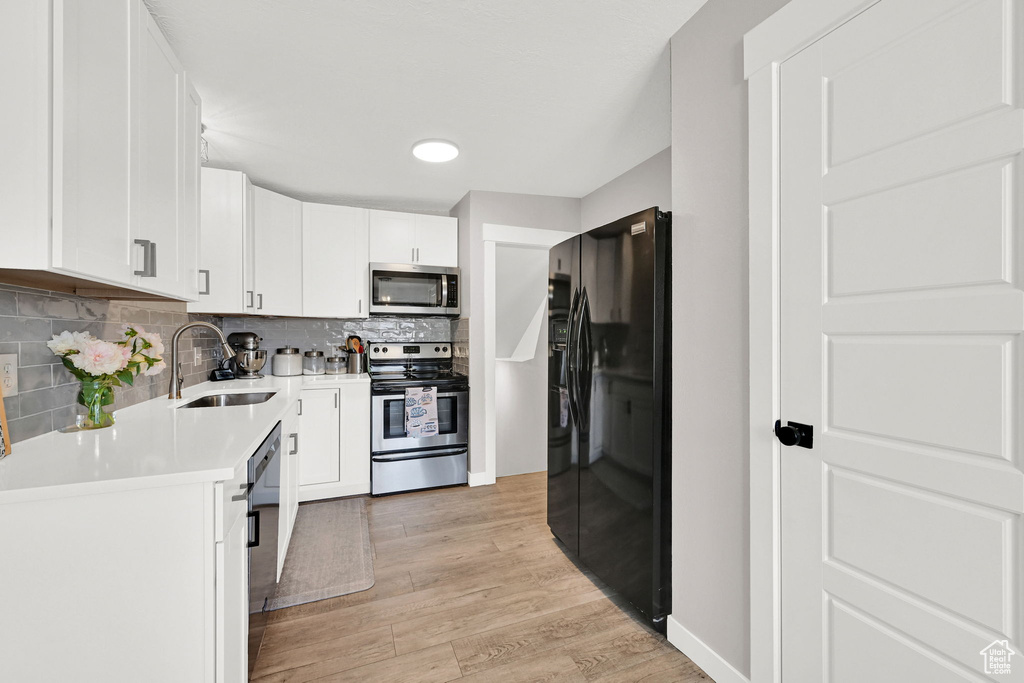 Kitchen featuring stainless steel appliances, a sink, light countertops, tasteful backsplash, and light wood finished floors
