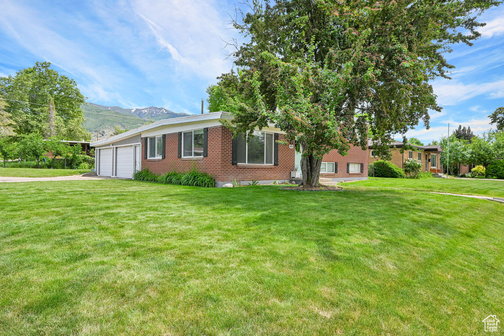 View of front of property featuring brick siding, a garage, asphalt driveway, a front yard, and a mountain view