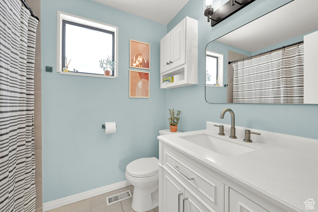 Full bath with toilet, healthy amount of natural light, vanity, and tile patterned flooring