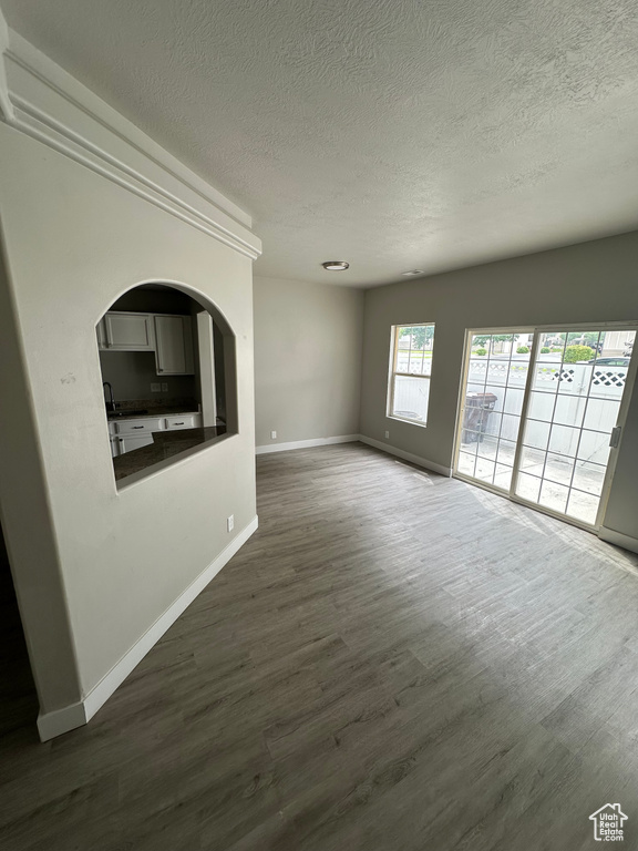 Unfurnished living room with a textured ceiling, baseboards, dark wood finished floors, and arched walkways