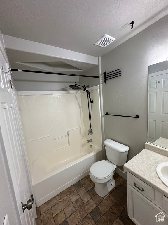 Bathroom featuring vanity, shower / washtub combination, stone finish floors, toilet, and a textured ceiling