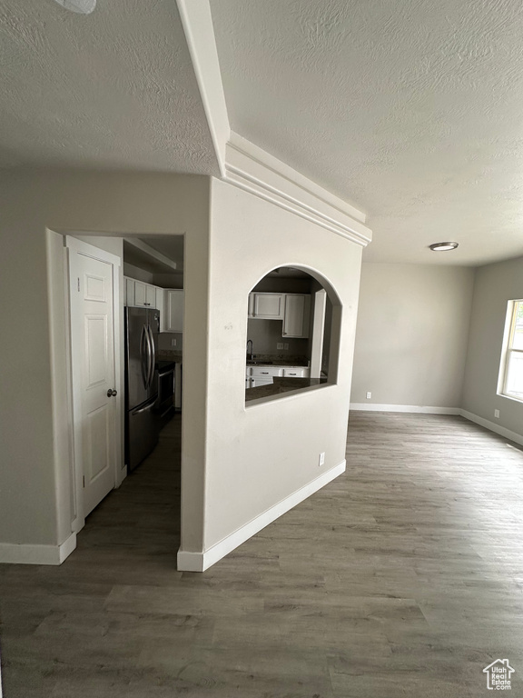 Unfurnished living room with a textured ceiling, dark wood-type flooring, baseboards, arched walkways, and a sink