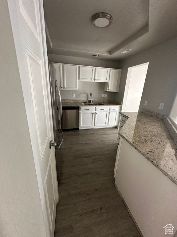Kitchen featuring stainless steel appliances, white cabinetry, a sink, dark wood finished floors, and light stone countertops