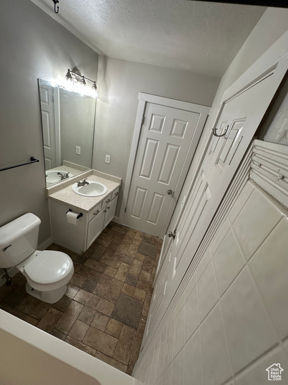 Bathroom with toilet, a textured ceiling, vanity, and stone finish floors