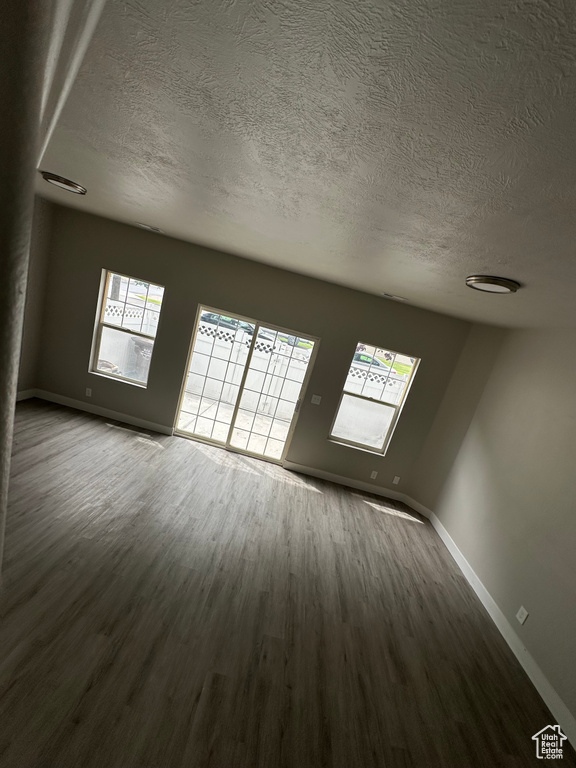 Unfurnished room featuring a textured ceiling, dark wood-style floors, and baseboards