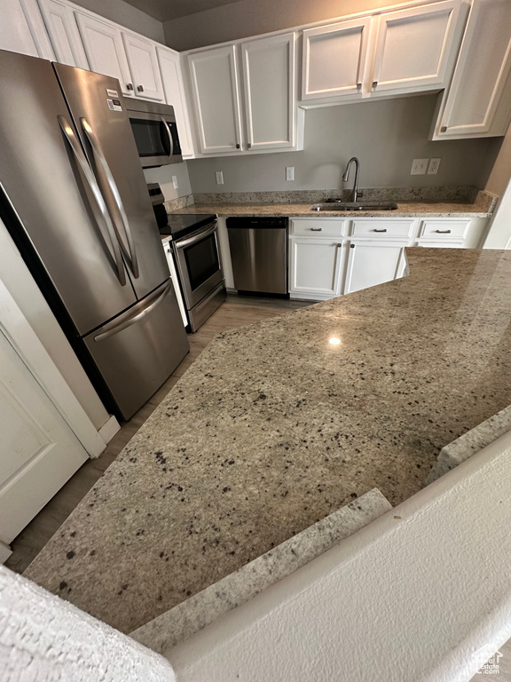 Kitchen with stainless steel appliances, a sink, white cabinetry, and light stone countertops