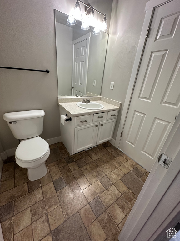 Bathroom featuring stone tile floors, vanity, toilet, and baseboards