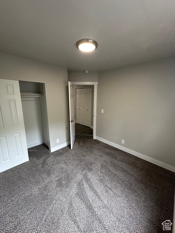 Unfurnished bedroom with dark colored carpet and baseboards