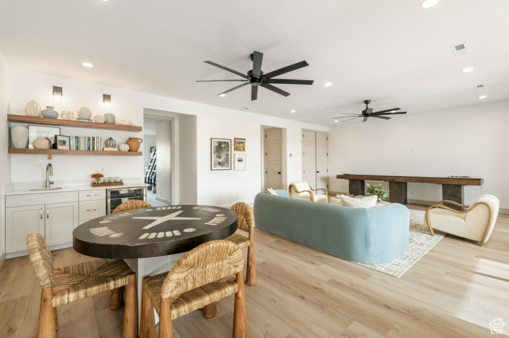 Dining space with beverage cooler, wet bar, ceiling fan, recessed lighting, and light wood-type flooring