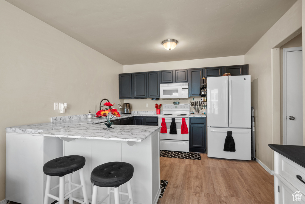 Kitchen featuring white appliances, a peninsula, a kitchen breakfast bar, light wood-style floors, and light stone countertops
