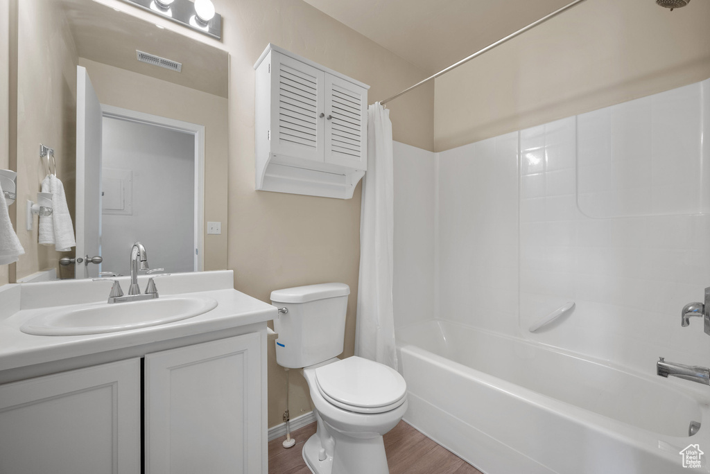 Bathroom featuring toilet, shower / tub combo with curtain, vanity, and wood finished floors