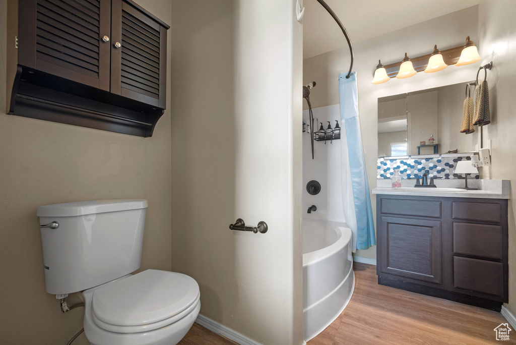 Bathroom featuring vanity, shower / bath combo with shower curtain, toilet, wood finished floors, and baseboards