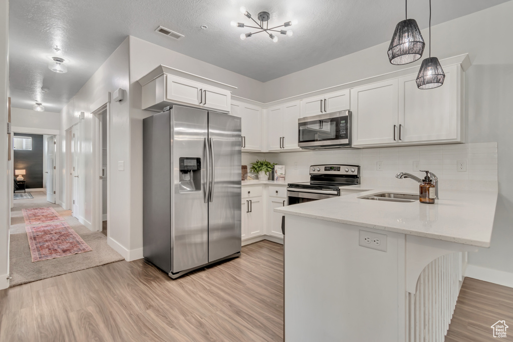 Kitchen with stainless steel appliances, a sink, light wood-style flooring, a peninsula, and white cabinets