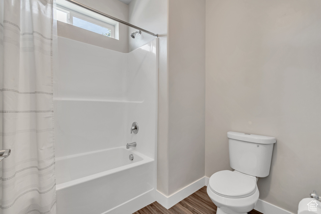Bathroom with baseboards, toilet, shower / bath combination with curtain, and wood finished floors
